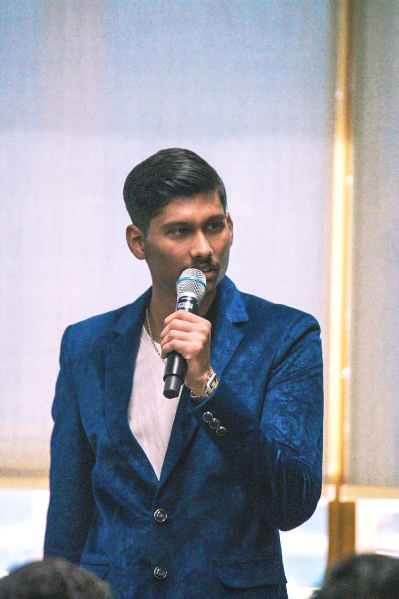 Kartik Bhattacharya speaking on stage with a microphone, delivering a cybersecurity keynote in a blue velvet blazer